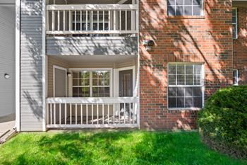 Private, fenced-in patio and balcony on a brick apartment building, overlooking a grassy area at Stonebriar Apartments.
